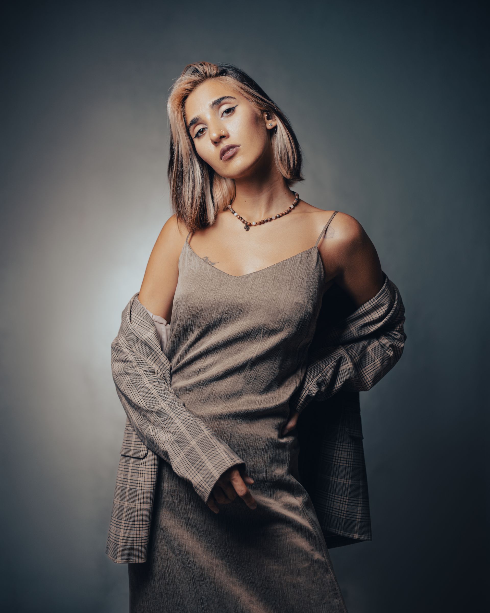 Fashion model in a slip dress with a plaid blazer draped off her shoulders in a studio portrait.