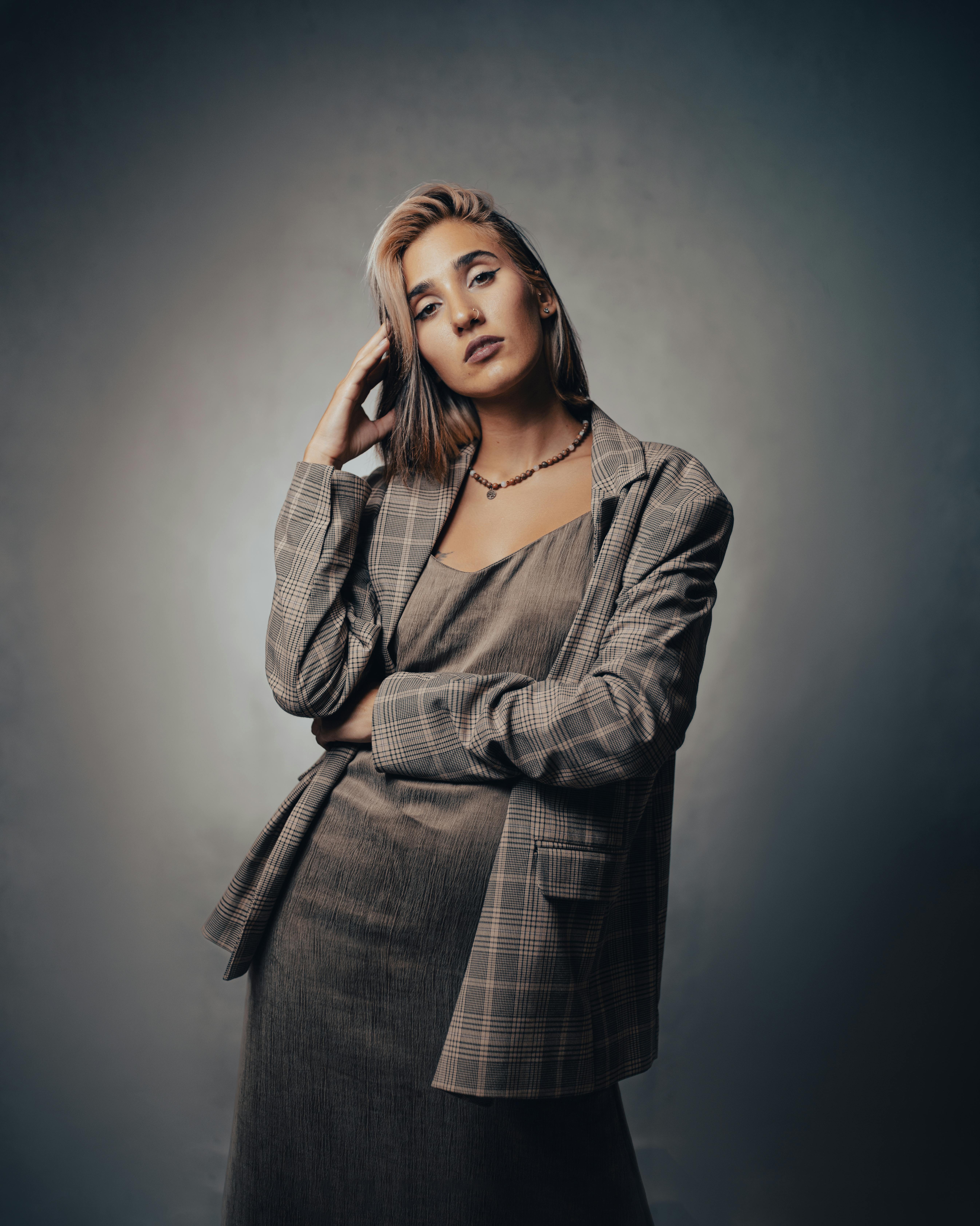 Free Portrait of a fashionable woman in a checked blazer, exuding elegance in a studio setting. Stock Photo