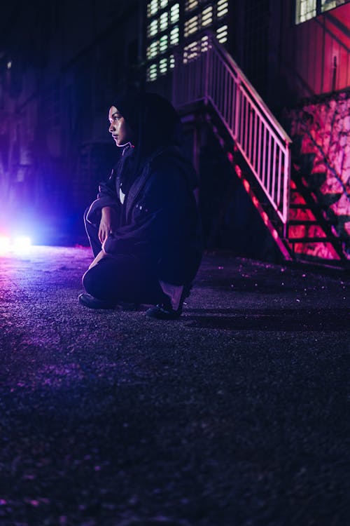 Woman Crouching on Street at Night