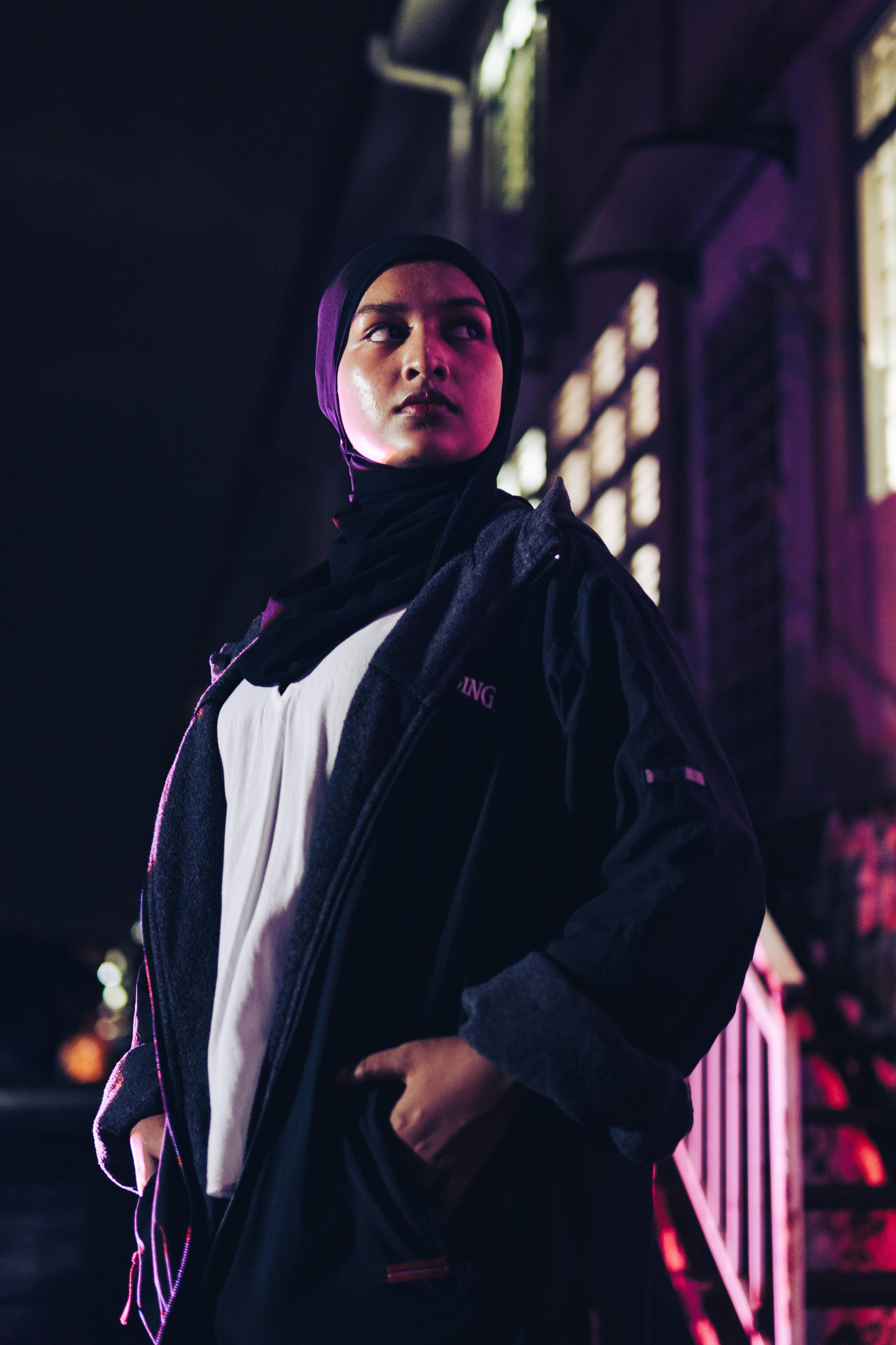 young woman in a hoodie and hijab standing in a dark interior