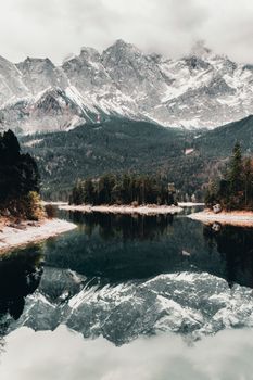 A serene view of snowcapped mountains reflecting in a still lake surrounded by lush trees.