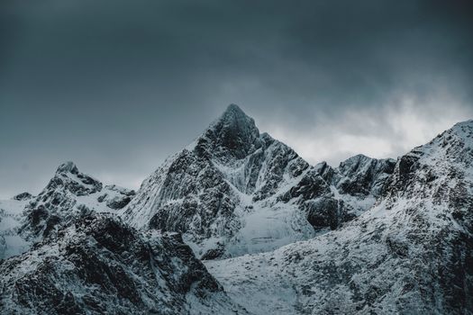 Stunning view of snow-covered rugged mountains under moody skies, capturing winter essence.