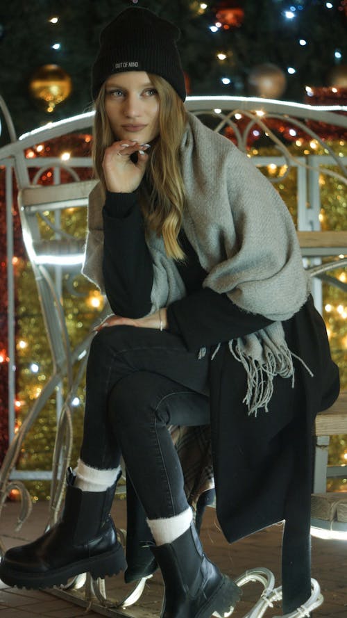 Young Woman in Warm Clothing Sitting on an Illuminated Christmas Decoration Outside 