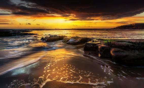 Golden hour at the rocky seaside, showcasing a vibrant sunset reflected on the calm ocean waters.