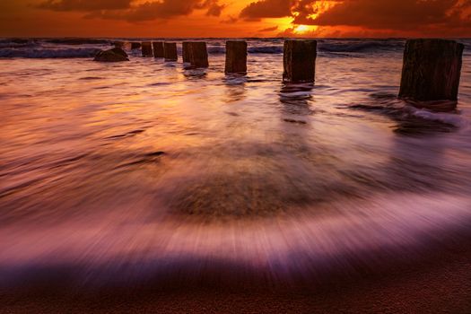 Stunning sunset at the beach with ocean waves and silhouetted wooden posts.