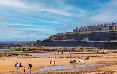 Free Families enjoying a sunny day at the picturesque Cullercoats Bay beach in England. Stock Photo
