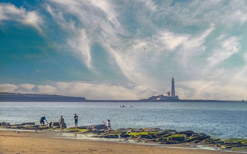 Free Families playing by a coastal lighthouse under dramatic skies, perfect for travel and nature themes. Stock Photo