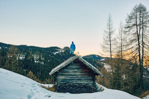 Man Standing atop Wooden Hut on Snow Covered Mountain Slope