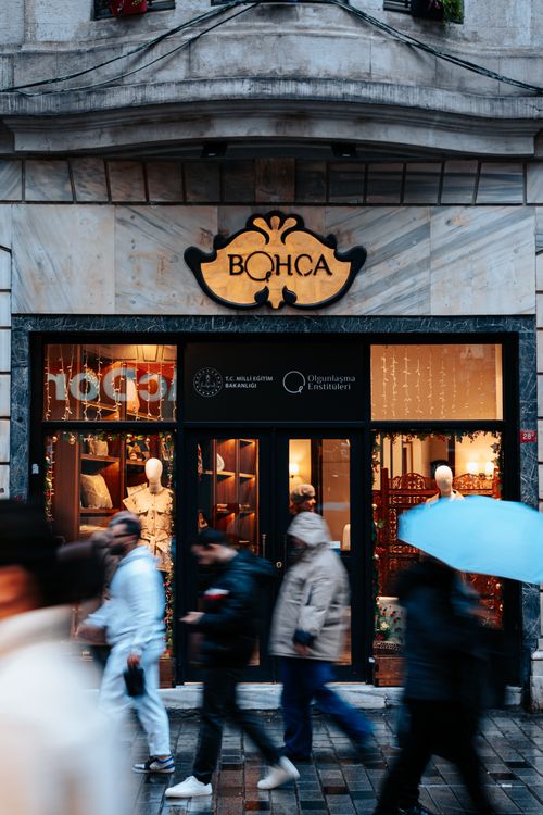 Free Blurred pedestrians walking past a Bohça store in an urban street scene, capturing city life. Stock Photo
