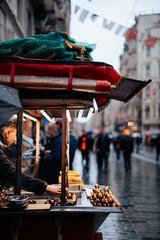 A street vendor sells chestnuts and corn on a rainy day in a lively urban area.