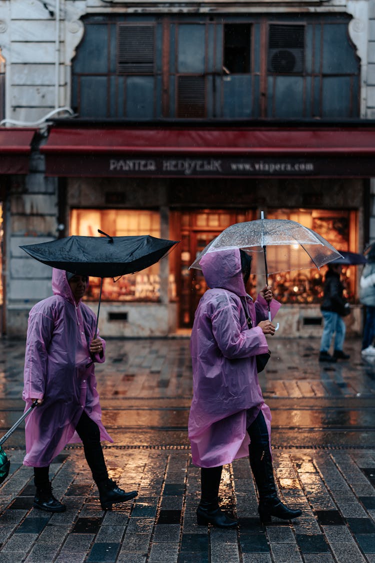 Pedestrians In Plastic Raincoats Under Umbrellas During Rain In City