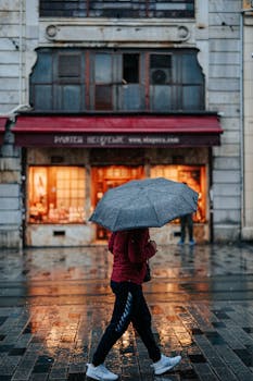 A person walks with an umbrella in a rainy city street in Turkey, reflecting vibrant urban life.