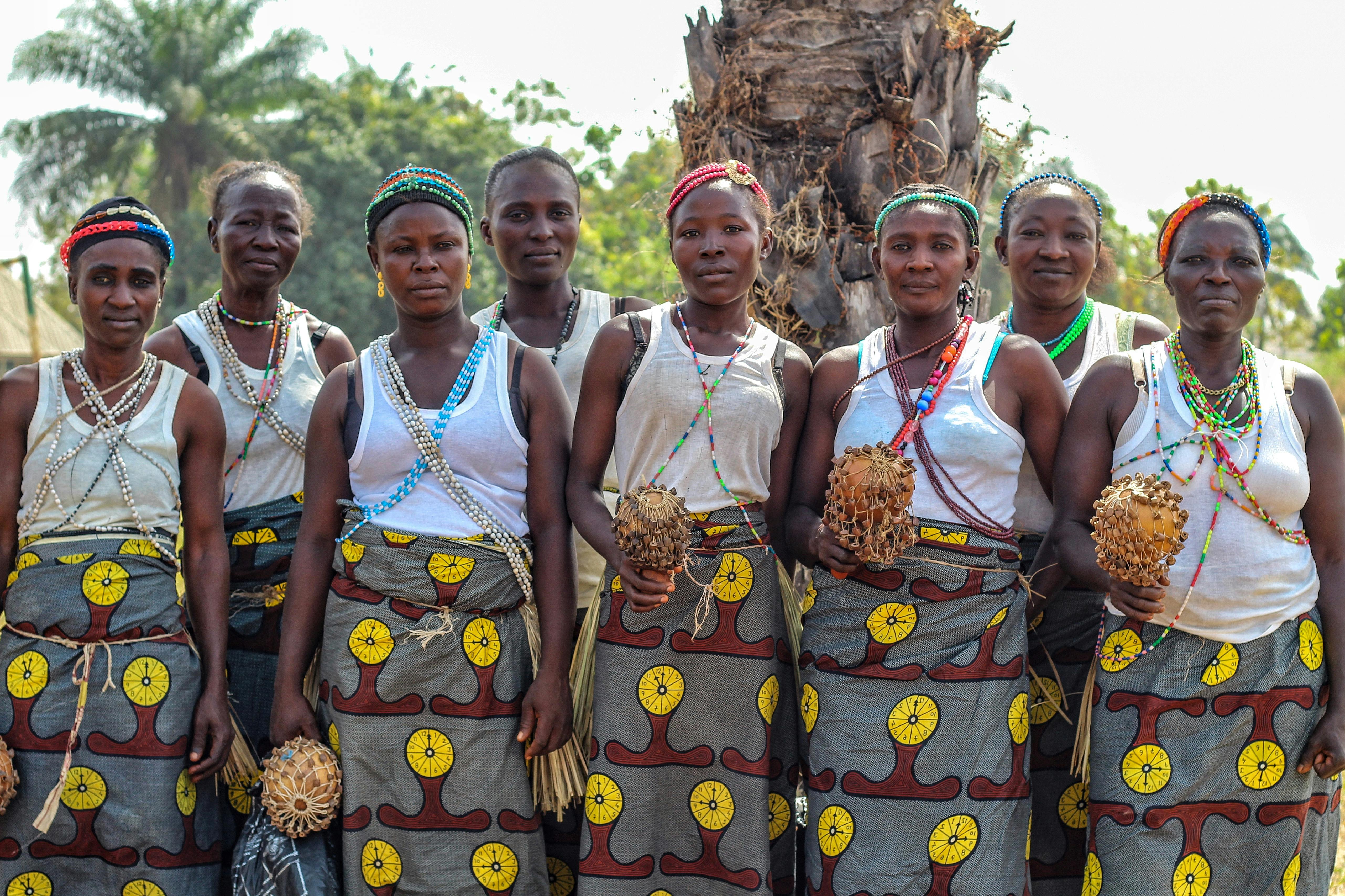 Ewe women weaving Kente cloth in a traditional village setting, vibrant colors, outdoor workshop
