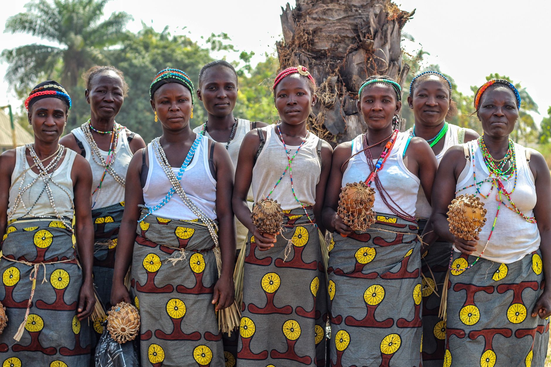 Group of African women in traditional attire with decorative beads, standing outdoors.