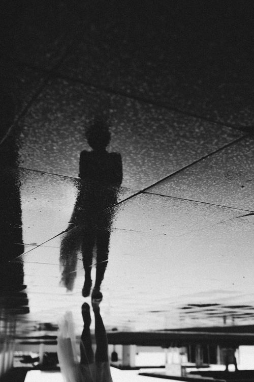 Free Artistic black and white photo capturing silhouette reflection on wet pavement outdoors. Stock Photo