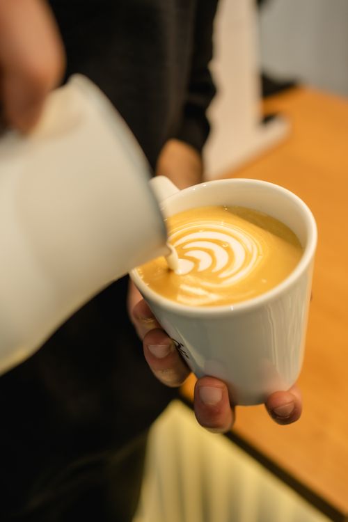 Free Close-up of expert barista pouring latte art in a warm café atmosphere. Stock Photo