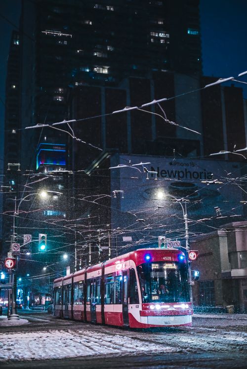 Free A red tram travels through a snowy city street at night, surrounded by tall buildings and glowing lights. Stock Photo