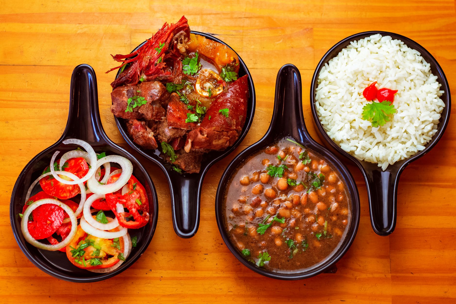 Bowl of vibrant green Peruvian goat stew with tender meat and vegetables in cilantro-based sauce, served with white rice