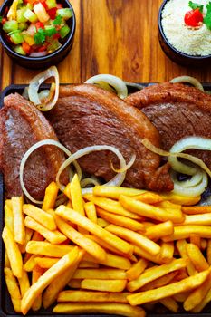 Sizzling steak with crispy fries and fresh salsa served on a wooden table.