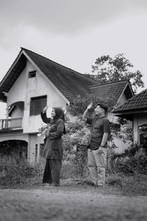Free A black and white photo of a man and woman waving outside in a village setting. Stock Photo
