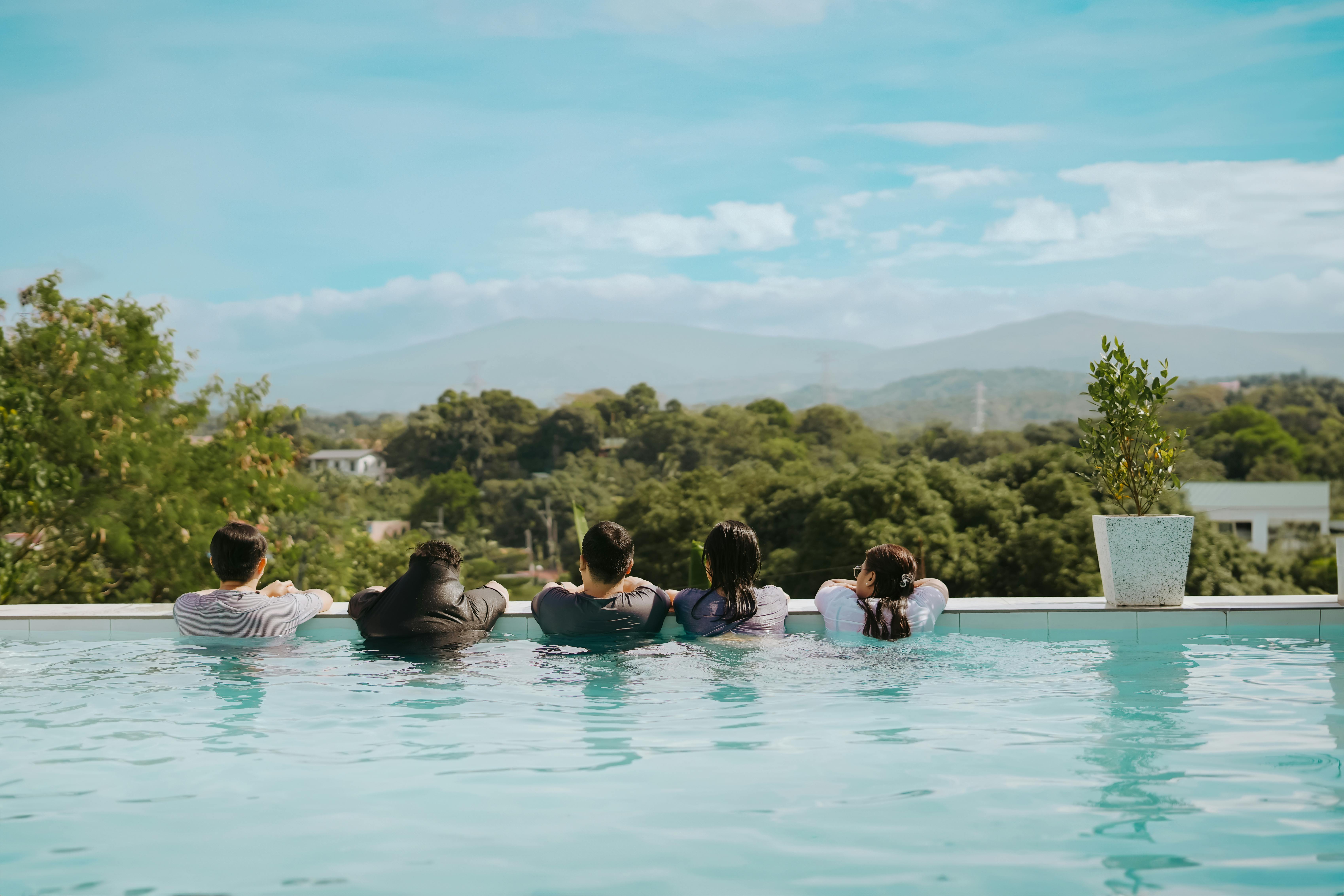 Group enjoying leisure time in an infinity pool overlooking lush green mountains.