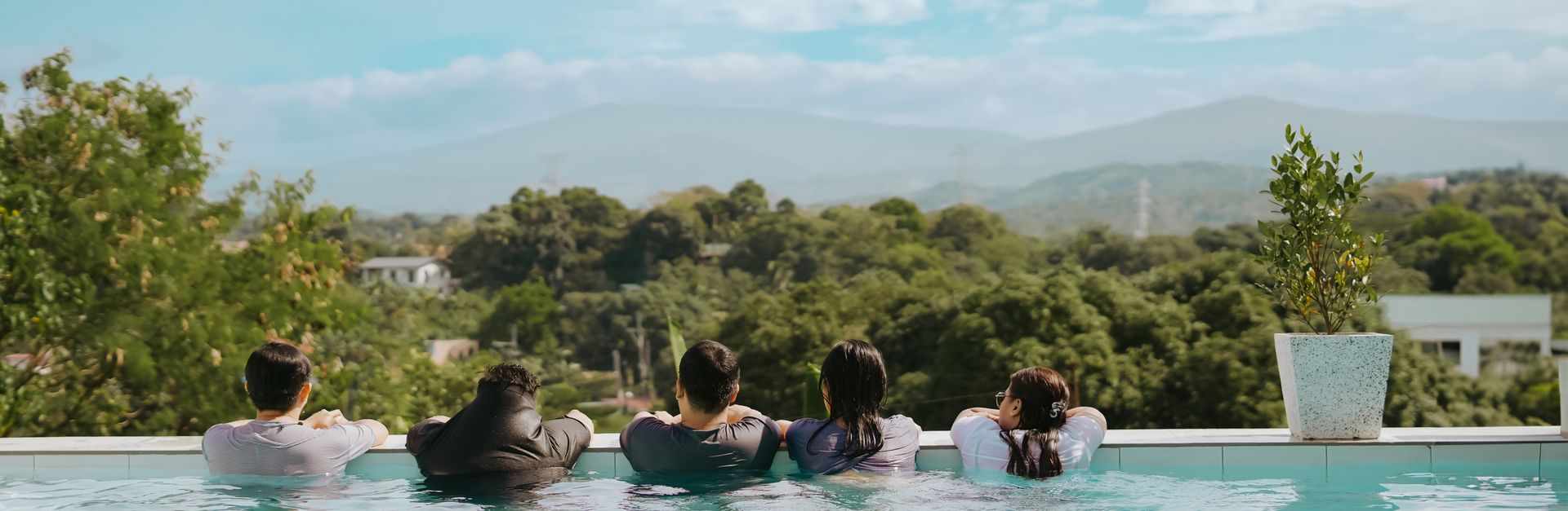 Group enjoying leisure time in an infinity pool overlooking lush green mountains.