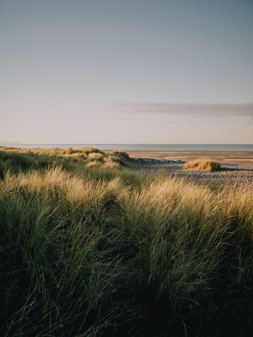 Free Peaceful dunes overlook the serene ocean at Rhyl, Wales, during sunset. Stock Photo