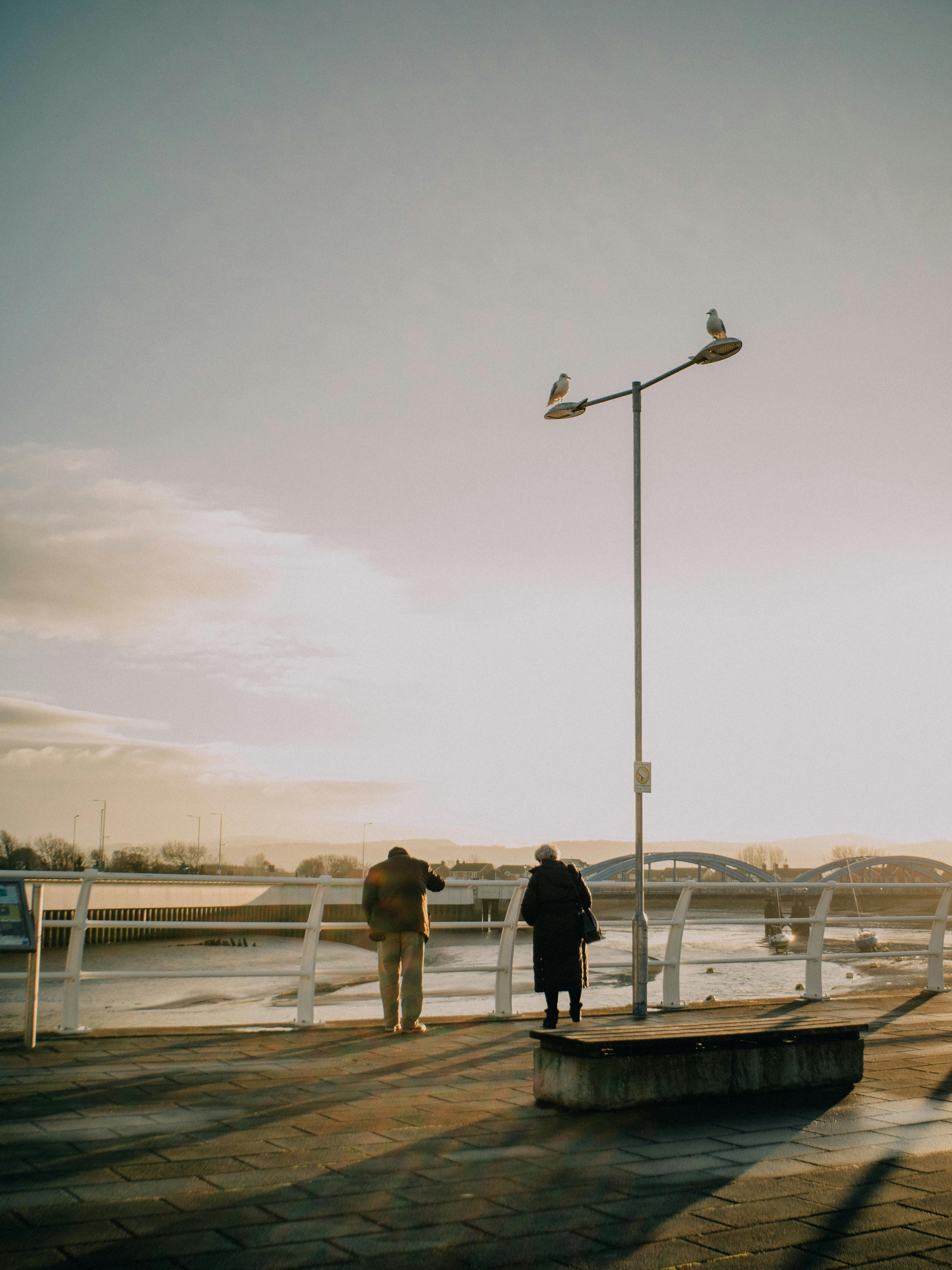 Tranquil scene of a senior couple enjoying the river view on a promenade during sunset.