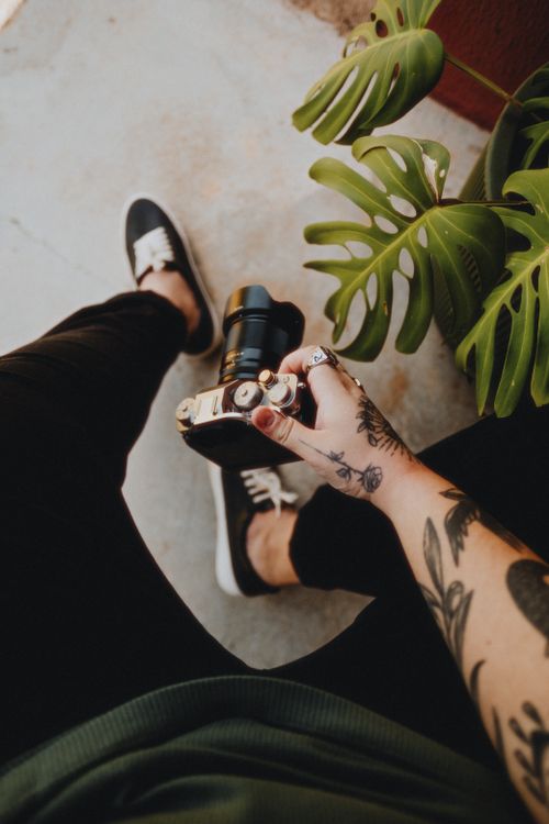 Free A person with tattoos holds a camera while sitting outdoors in Mirassol, Brasil. Stock Photo