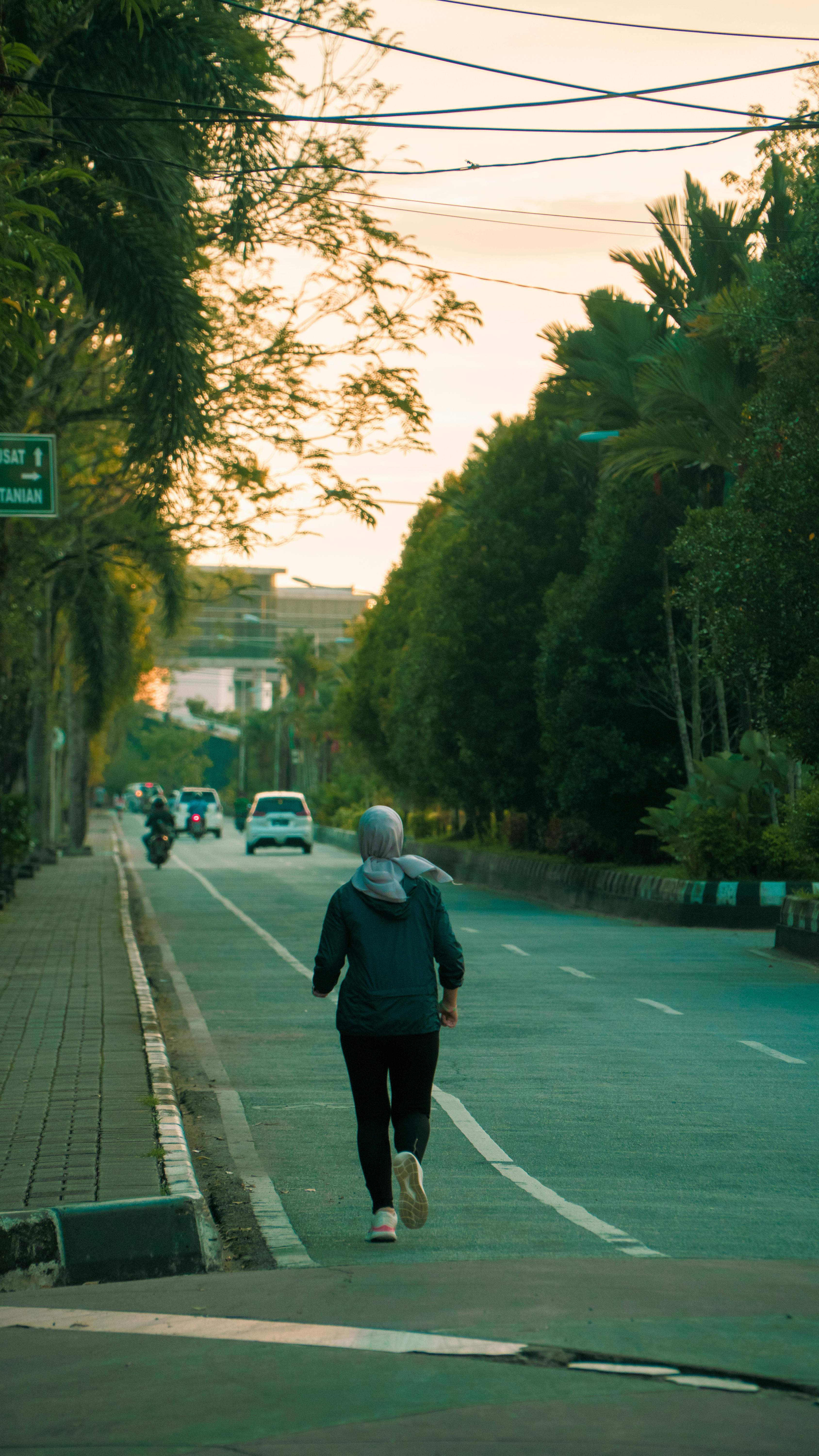 A woman jogs down a quiet city street with trees lining the path during sunrise.