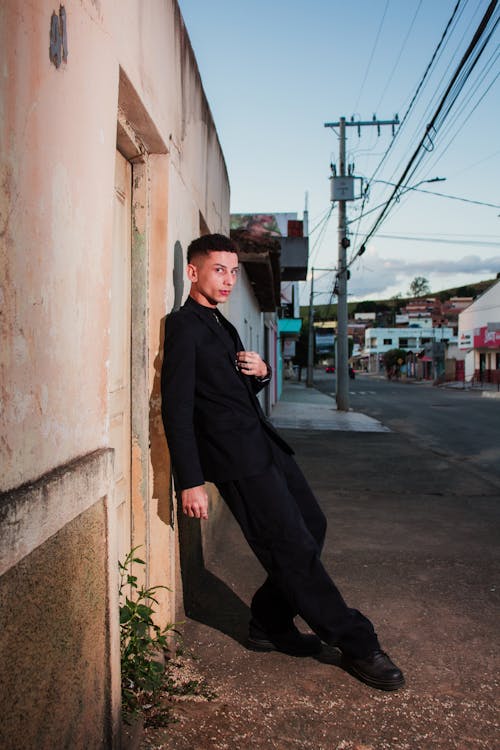 Young Man in Black Suit Posing by Wall in City