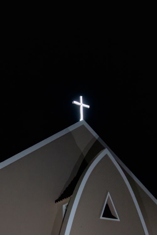 Free Vertical shot of church facade with illuminated cross against a dark night sky, symbolizing faith and tranquility. Stock Photo