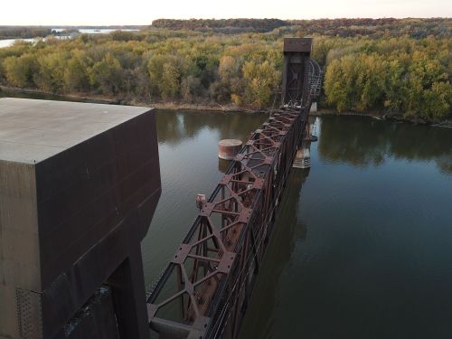 Free Drone shot of a steel railroad bridge crossing a river through a lush forest. Stock Photo