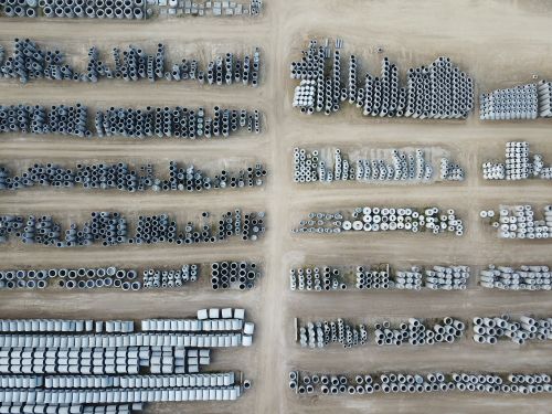 Free Drone aerial shot of industrial pipes stored in rows on a dirt lot. Stock Photo