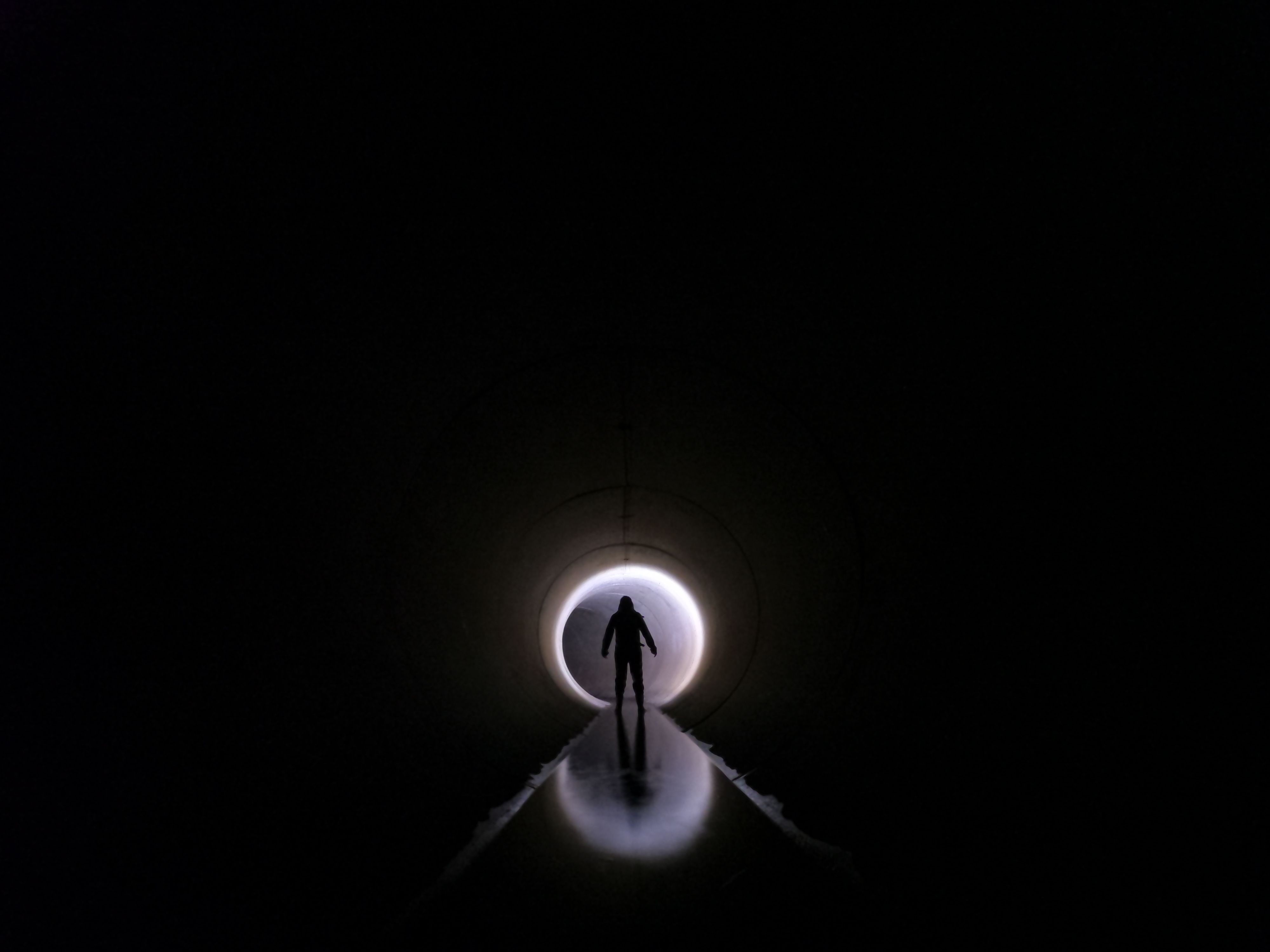 Dramatic silhouette of an individual standing in a dark tunnel with light at the end.