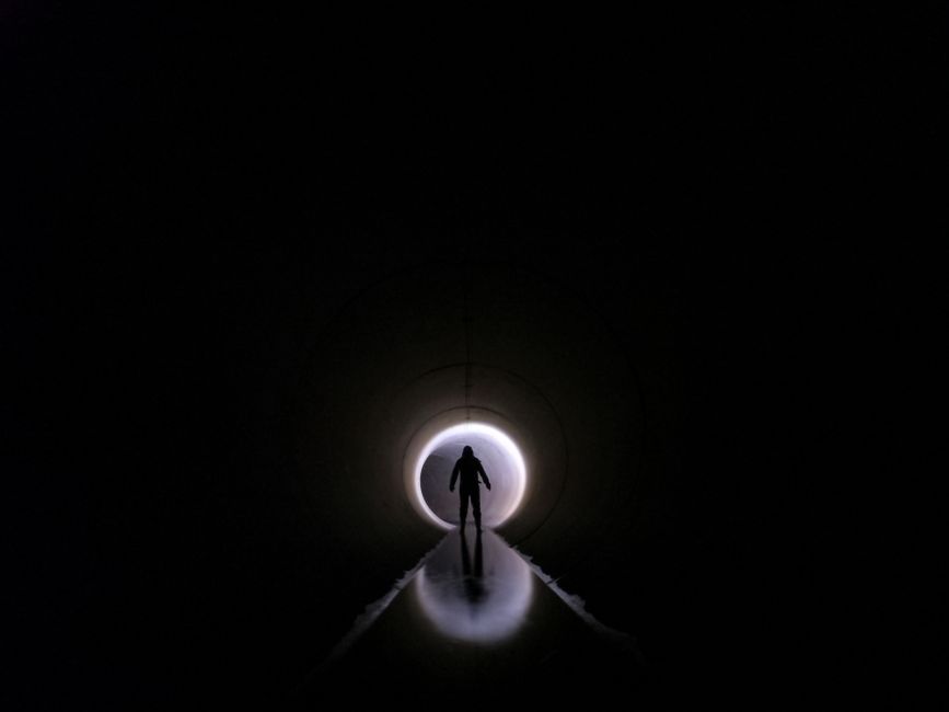 Dramatic silhouette of an individual standing in a dark tunnel with light at the end.
