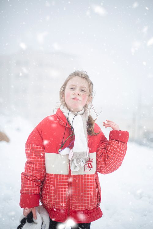 Free Young girl in red jacket enjoying snowfall in Amman, Jordan during winter. Stock Photo