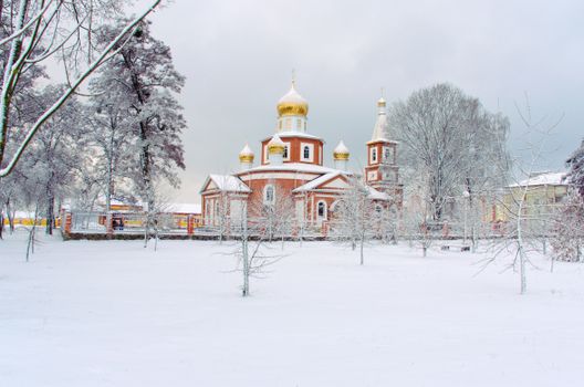 A serene winter scene of a snow-covered Orthodox church with golden domes surrounded by trees.