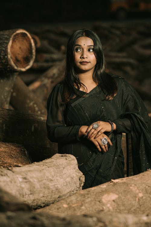 Young Woman in a Dark Saree Standing among Tree Logs 