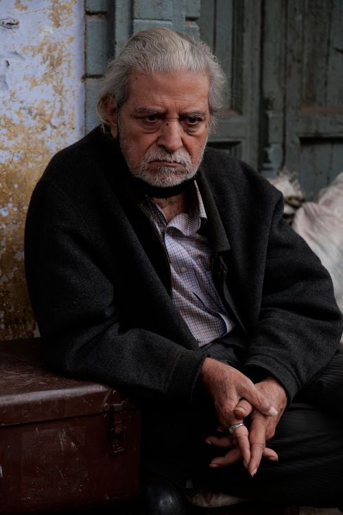 Free Pensive elderly man sitting against an aged wall in the streets of Delhi, India. Stock Photo