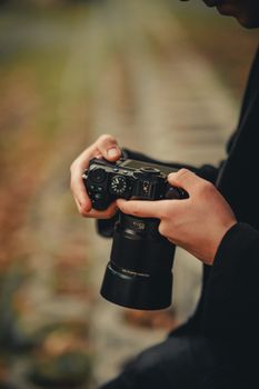 A person adjusting settings on a DSLR camera outdoors in a blurred natural setting.