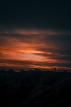 Stunning silhouette of a car and person against a vibrant sunset with dramatic clouds.