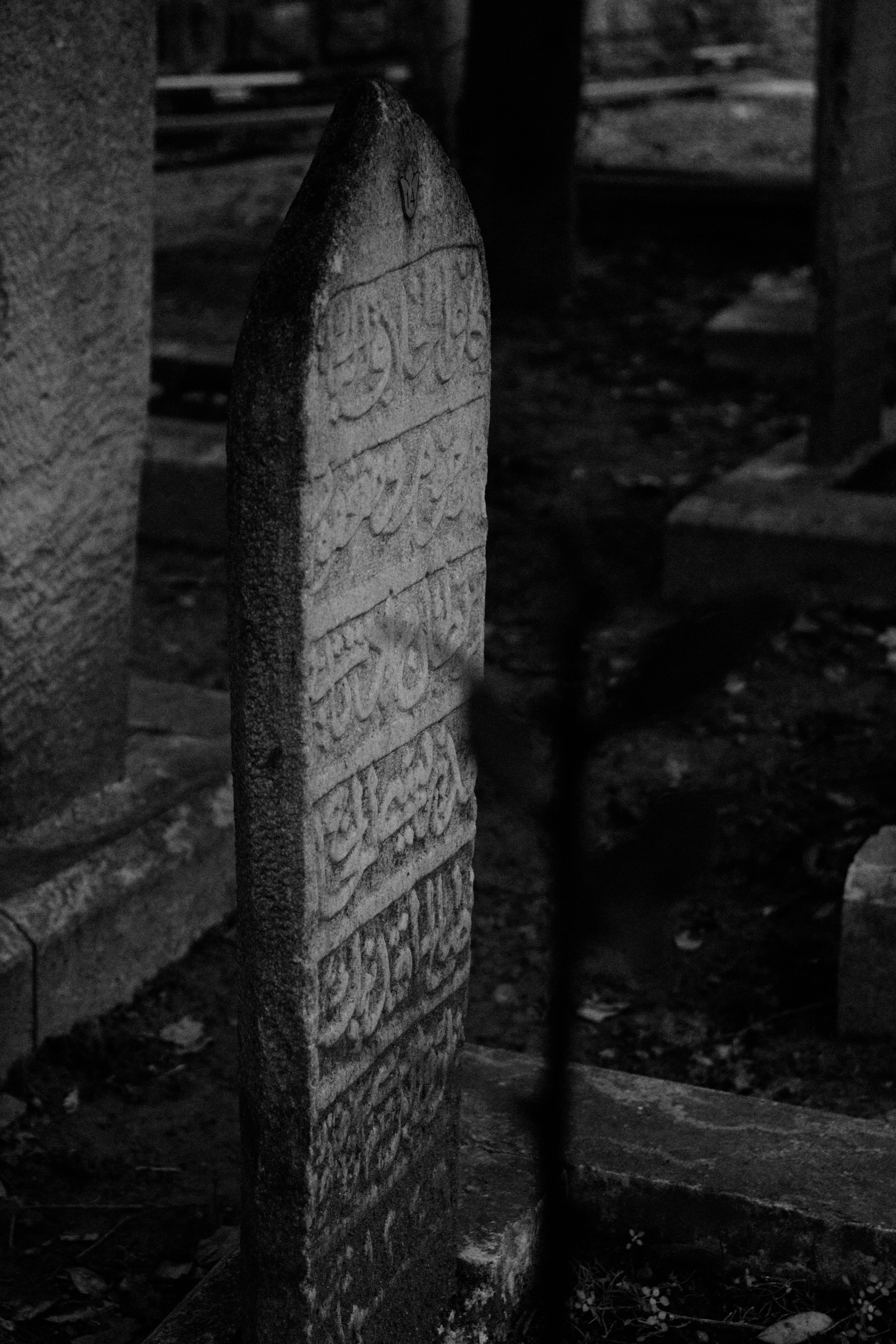A historic Islamic tombstone with intricate script, captured in a moody black and white cemetery setting.