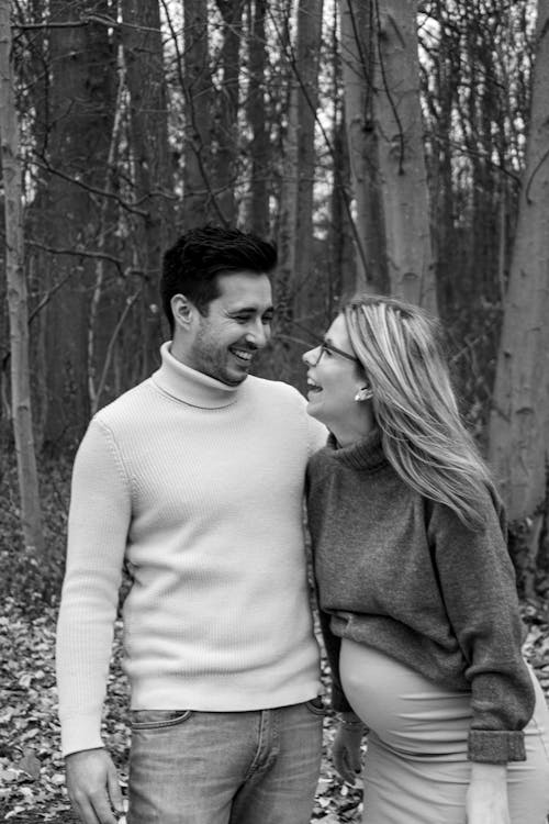 Black and White Photo of a Pregnant Woman Standing with a Man in a Forest