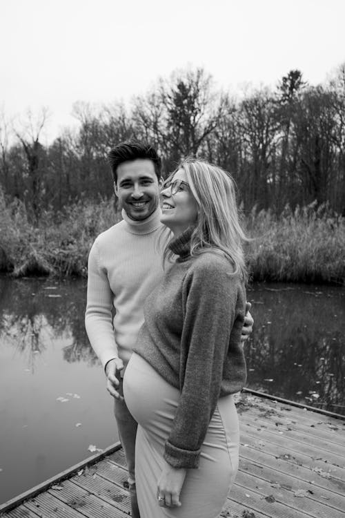 Black and White Photo of a Pregnant Woman Standing with a Man on a Jetty