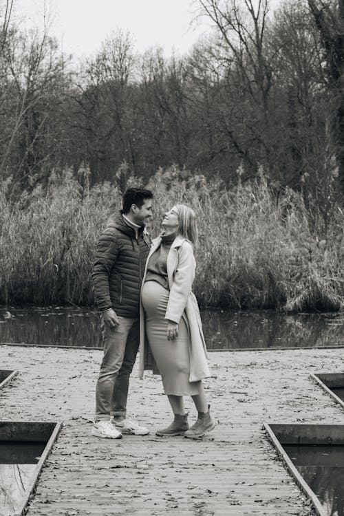 Black and White Photo of a Pregnant Woman Standing with a Man on a Jetty