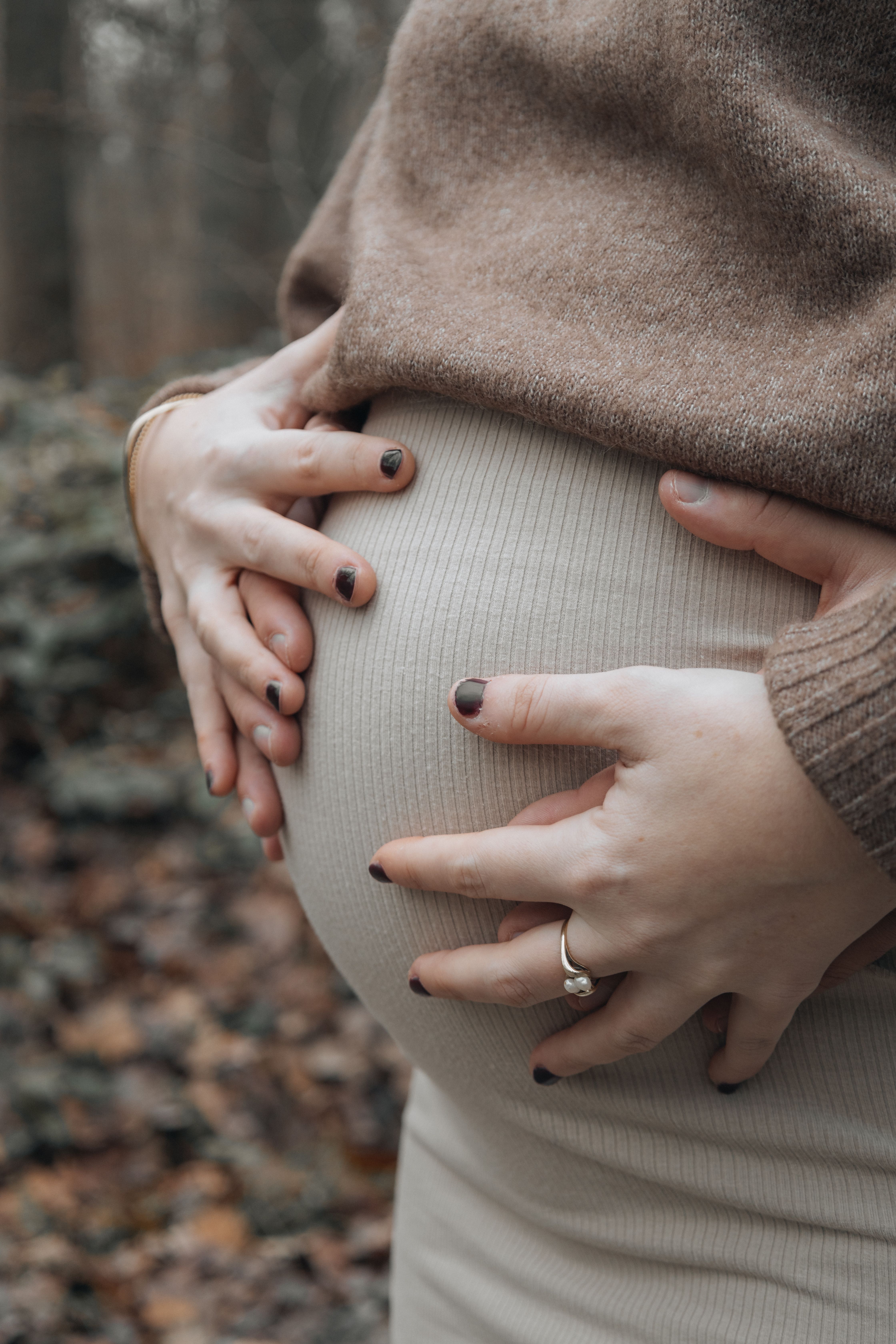 Expectant couple gently holding the pregnant belly in a serene outdoor setting. - Fotografer Sidoarjo