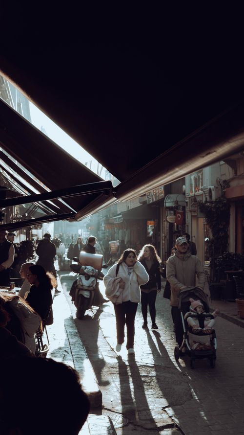 Free A bustling urban street with pedestrians casting long shadows under bright sunlight, capturing everyday city life. Stock Photo