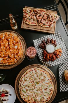 A tempting top-down view of pizzas, wings, and drinks on a restaurant table.