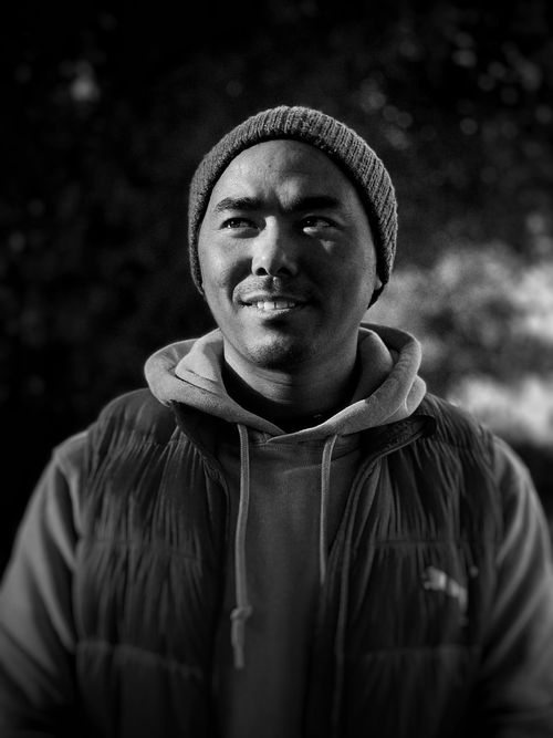 Free A black and white portrait of a smiling man wearing a beanie and hoodie outdoors. Stock Photo